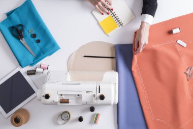 Dikiş makinesi yakınındaki kırmızı malzeme tutan kadın