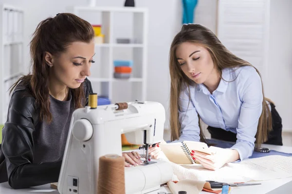 Mädchen in Schwarz näht. Ihr Kollege schaut sich Notizen an — Stockfoto