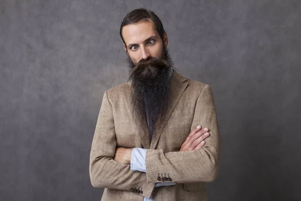 Businessman with long beard wearing beige suit is standing against gray background and goofing around — Stock Photo, Image