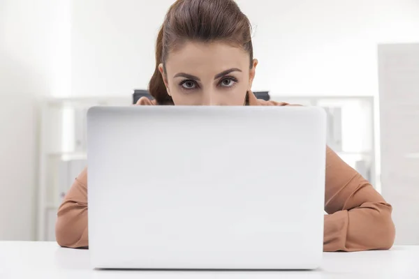 Frau in brauner Bluse versteckt sich hinter ihrem Laptop — Stockfoto
