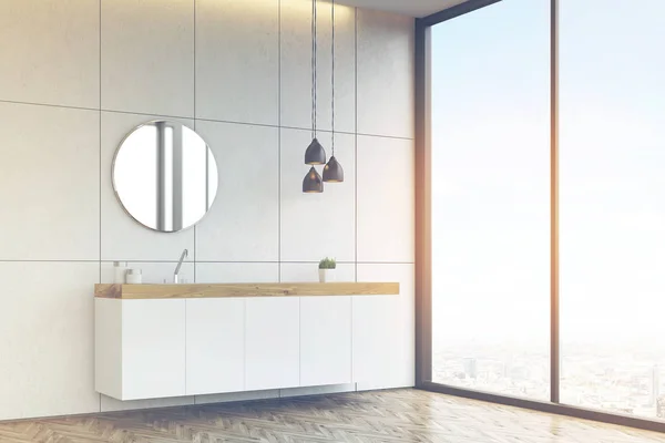 Side view of a bathroom sink with round mirror on tiled wall, to