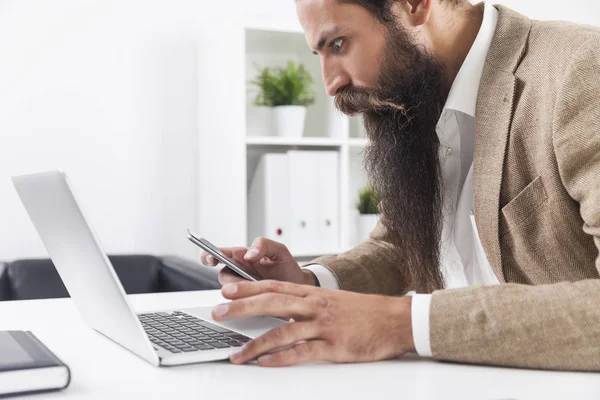 Vista lateral do homem de negócios com barba longa olhando para o seu celular pho — Fotografia de Stock