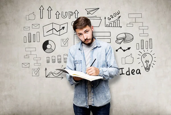 Empresario barbudo con un cuaderno cerca de una pared de hormigón con un — Foto de Stock