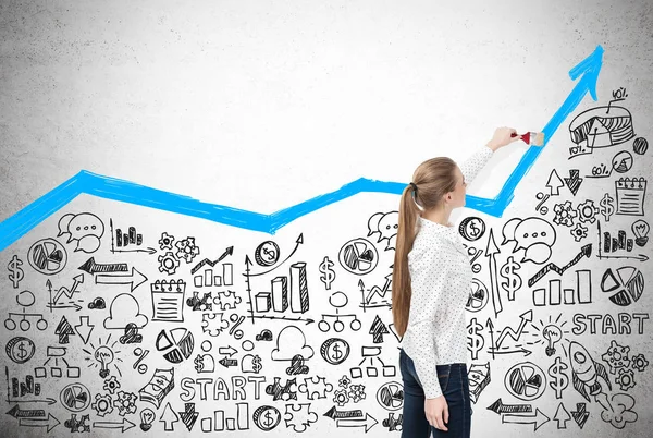 Woman drawing a blue graph on concrete wall with sketches — Stock Photo, Image