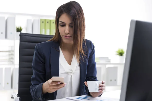 Affärskvinna med sin mobiltelefon och en kopp kaffe — Stockfoto