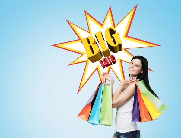 Woman with multiple shopping bags near a big sale poster on a bl — Stock Photo, Image