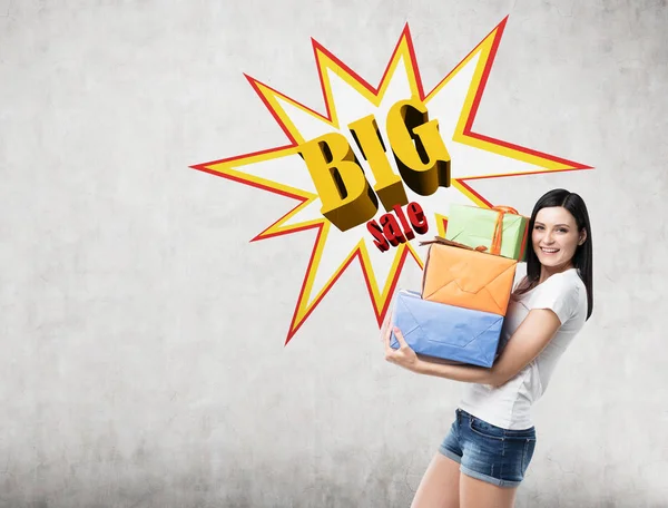 Vrouw met presenteert in de buurt van een betonnen muur met grote verkoop poster — Stockfoto