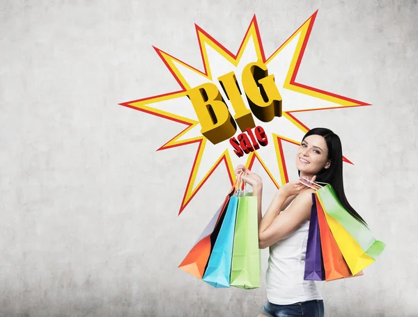 Woman with multiple shopping bags near a big sale poster — Stock Photo, Image