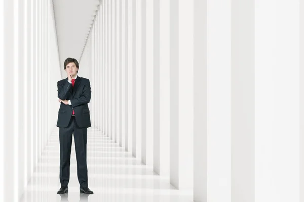 Молодой бизнесмен в костюме стоит в белом коридоре и думает: . — стоковое фото