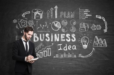 Bir defter ile sakallı işadamı duran bir blackboard iş fikir simgelerle yakınındaki yazma.