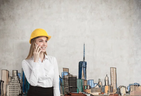 Ritratto di una donna d'affari bionda con un cappello giallo e che parla sul suo smartphone mentre si trova vicino a un muro di cemento con un panorama colorato della città. Scherzi? . — Foto Stock