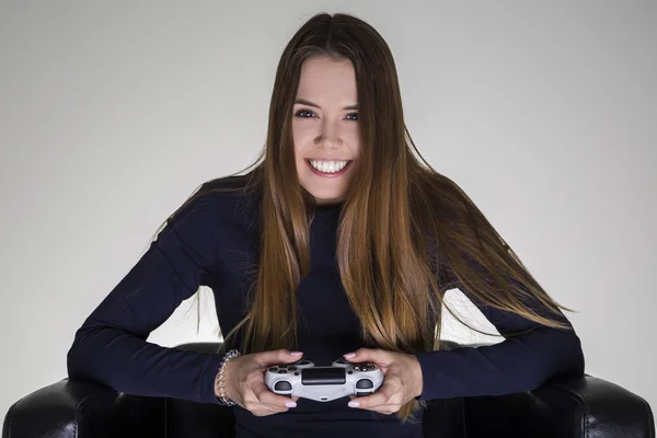 Portret van een gelukkig bepaald meisje zittend in een lederen fauteuil en houden van een video game controller. — Stockfoto