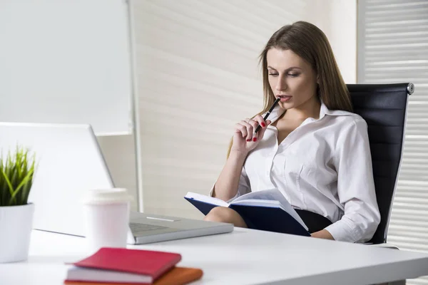 Närbild av en allvarlig och vacker affärskvinna bär en vit blus och sitter vid sitt skrivbord med en anteckningsbok och glasögon. Håna upp. — Stockfoto