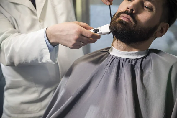 Close up of a serious brown haired businessman having his beard combed and trimmed in a barber shop. — Stock Photo, Image