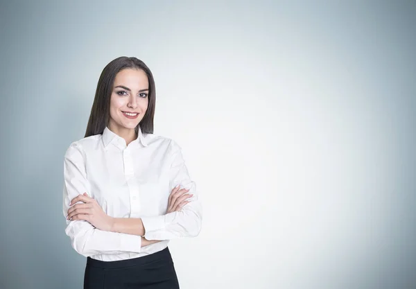 Retrato de uma empresária sorridente de pé com os braços cruzados perto de uma parede cinza e olhando para o espectador com confiança . — Fotografia de Stock