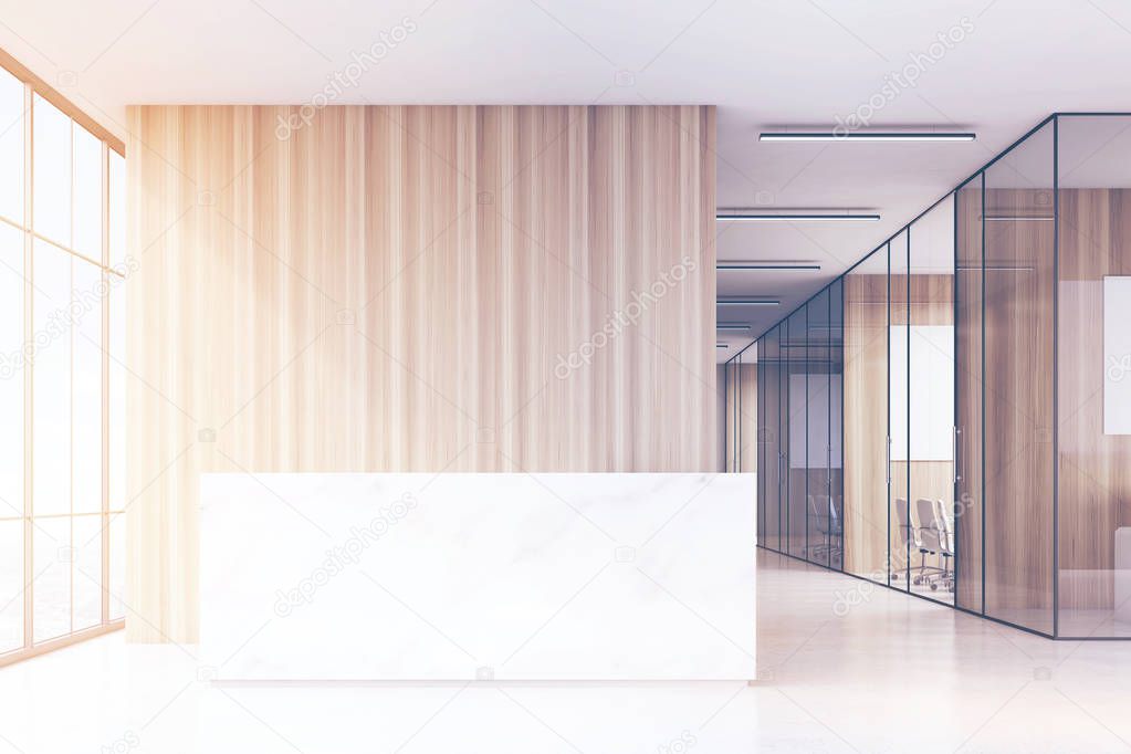 Office hall with panoramic windows and light wooden and glass walls of meeting rooms. There is a marble reception counter in the left part.