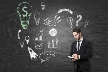 İş notları alarak genç iş adamı. Kara tahta arka plan çizimleri ile üzerinde duruyor. Kavram başlatmak