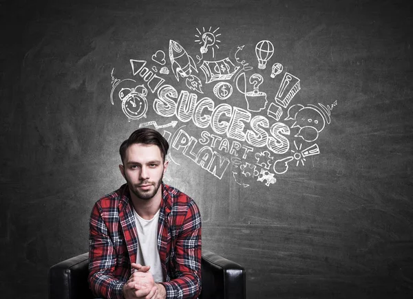 Young european guy in casual shirt sitting on blackboard background with business sketch. Success concept — Stock Photo, Image