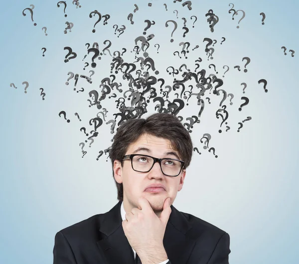 Thinking man in glasses, question marks, gray wall — Stock Photo, Image