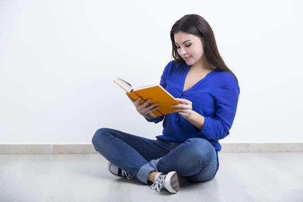 Улыбающаяся девушка в джинсах читает книгу — стоковое фото