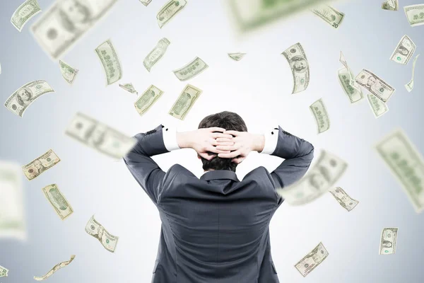 Man with hands behind head and dollars falling — Stock Photo, Image
