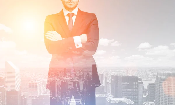 Doppelbelichtung eines bis zur Unkenntlichkeit gekreuzten Geschäftsmannes, der vor einem Stadtpanorama steht, getöntes Bild, Attrappe — Stockbild Mann mit gekreuzten Armen und eine Stadt, durchtrainiert — Stockfoto