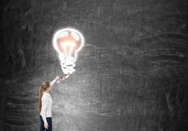 Woman drawing light bulb on blackboard
