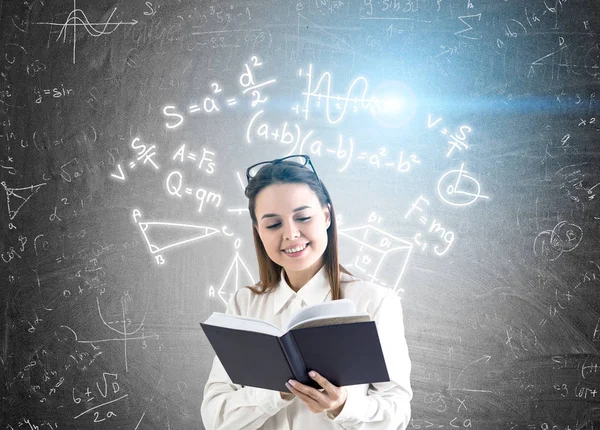 Mujer con libro y fórmulas en pizarra — Foto de Stock