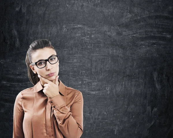 Femme pensive dans des lunettes près d'un tableau noir — Photo