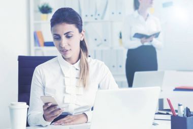 Ciddi kadın ofiste telefon bakarak
