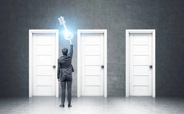 Businessman holding a giant key near doors — Stock Photo, Image