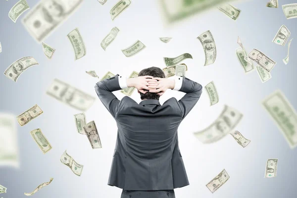 Businessman with hands behind head in money flow — Stock Photo, Image