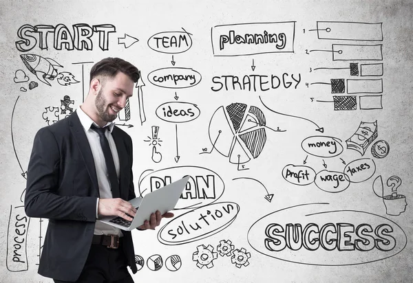 Un hombre de negocios sonriente con un portátil y un boceto de startup — Foto de Stock