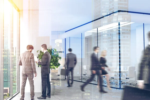 Företagets anställda är promenader och talar i ett modernt kontor med vit och glasväggar, betonggolv och panoramafönster. — Stockfoto