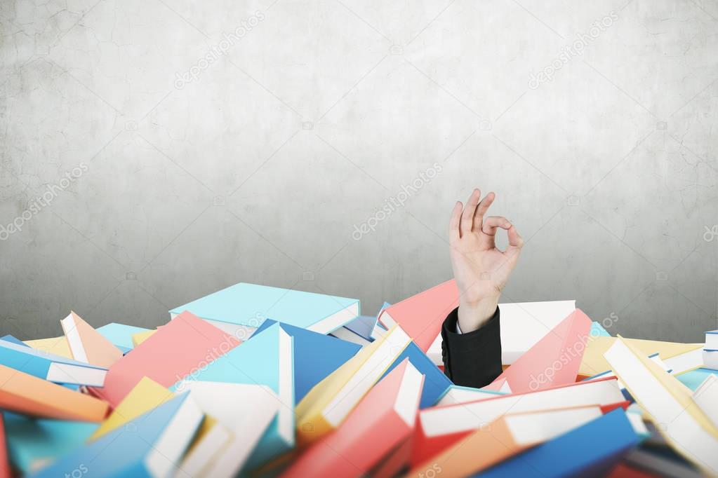 Man s hand making ok sign, pile of books