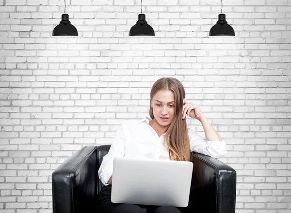 Blonde woman in armchair, laptop, brick — Stock Photo, Image