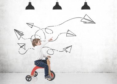 Kağıt uçaklar gösterilen sevimli çocuk bir üç tekerlekli bisiklet üzerinde