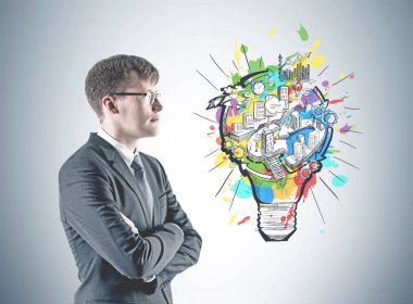 Kendine güvenen genç işadamı yan görünüm bir takım elbise ve gözlük ve ile ayakta silah mesafe içine bakarak geçti. Gri bir duvar üzerine işletme fikir kroki ile yakın duruyor.