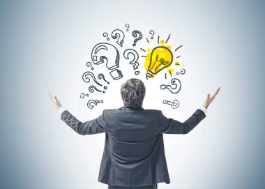 Arkadan görünüş genç başarılı işadamı ile ayakta eller havaya bir iş zaferini kutluyor. Soru işaretleri ve gri bir duvar bir ampul