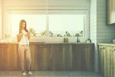 Ahşap mutfak tezgahı ile tropikal bir manzara ile büyük bir pencere altında duran bir yerleşik lavabo. Smartphone 3d render sahte tonlu görüntü çift pozlama kadar bir kadınla