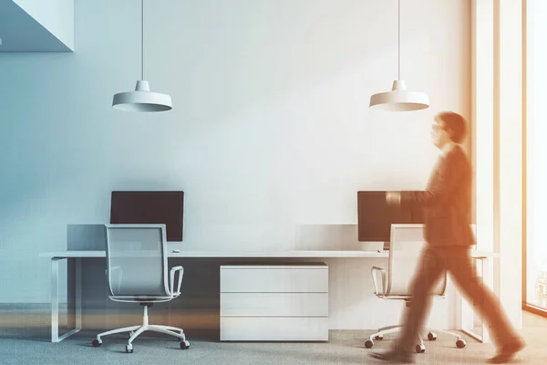 White wall office interior with loft windows, a dark gray carpet on the floor and rows of computer tables. A businessman 3d rendering mock up toned image double exposure blurred