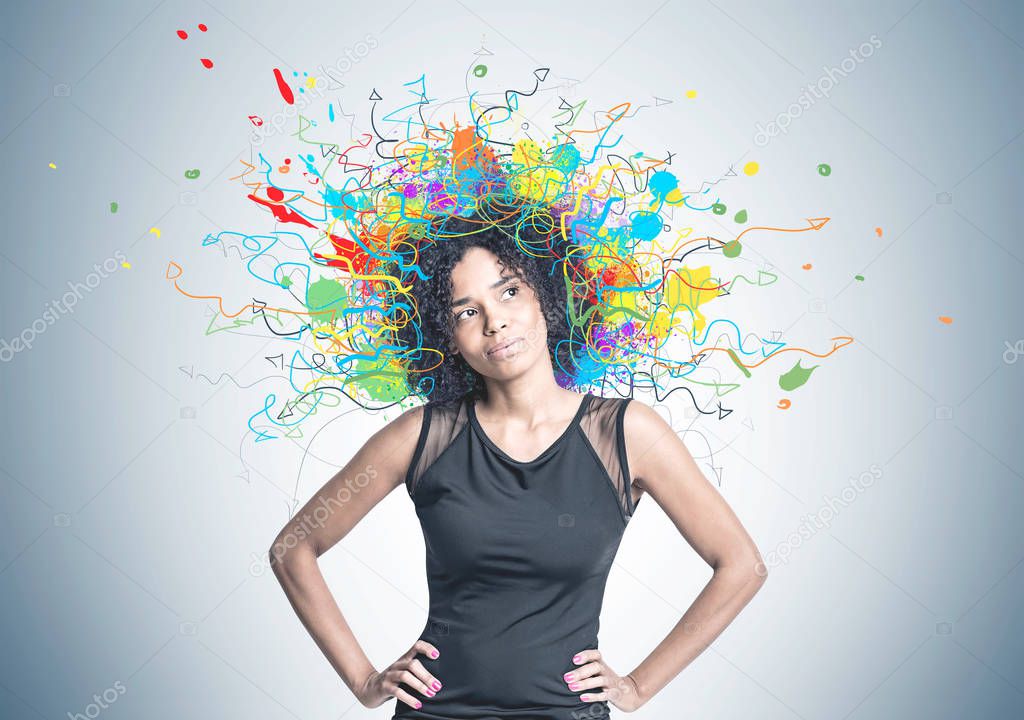 Gorgeous young African American woman wearing black jeans is standing with her hands on the waist and thinking. A gray wall background with many colorful arrows and splashes