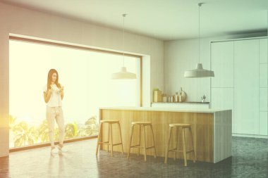 Barlı ve tabureli beyaz mutfakta bir kadın.