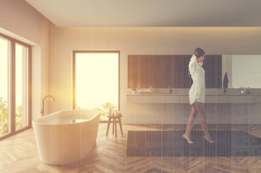 Genç bir kadın beyaz banyoda yürüyor.