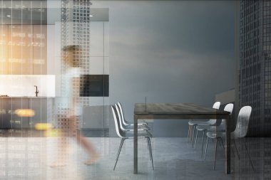 Gri mutfakta ve yemek odasında yürüyen bir kadın.