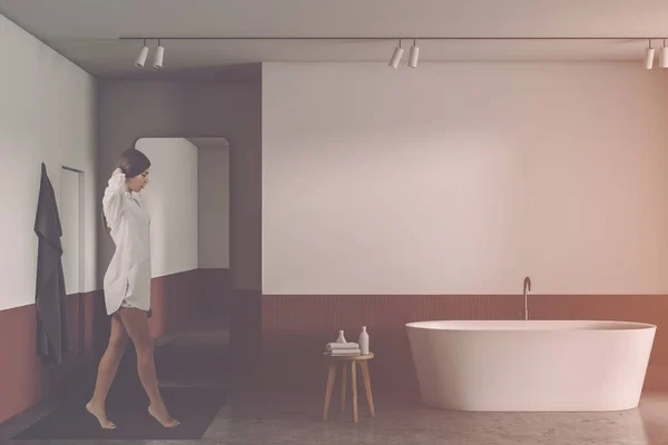 Mulher andando em banheiro branco e vermelho com banheira — Fotografia de Stock
