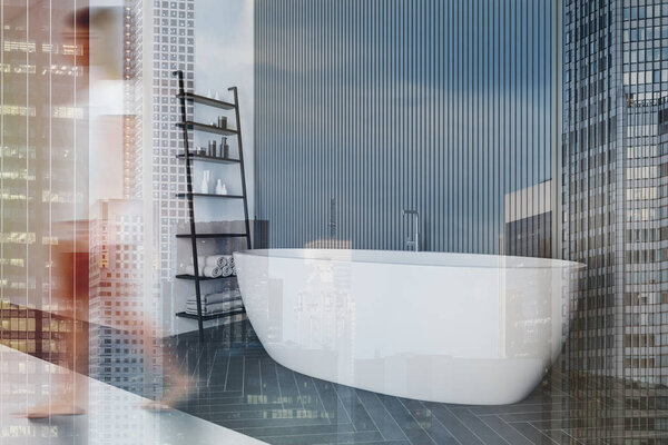 Blurry young woman walking in modern bathroom with gray and white walls, black wooden floor, comfortable bathtub and shelf with towels. Toned image double exposure