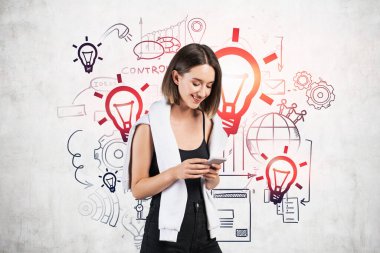 Üzerinde yaratıcı iş fikri çizimi olan beton duvarın yanında akıllı telefon kullanan sıradan giyinmiş neşeli genç bir kadın. Başlangıç ve yaratıcılık kavramı
