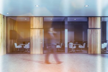 Bulanık işadamı çalışma tarzı ofisinde gri ve ahşap duvarlar, fayanslı döşemeler ve dizüstü bilgisayarlı yuvarlak masalarla yürüyor. Duvarda televizyon var. Tonu ayarlanmış resim