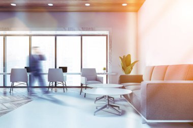 Bulanık genç işadamı, beyaz duvarları olan lüks ofis bekleme odasında yürüyor, sehpanın yanındaki rahat gri kanepe ve beyaz mermer bilgisayar masası. Tonu ayarlanmış resim